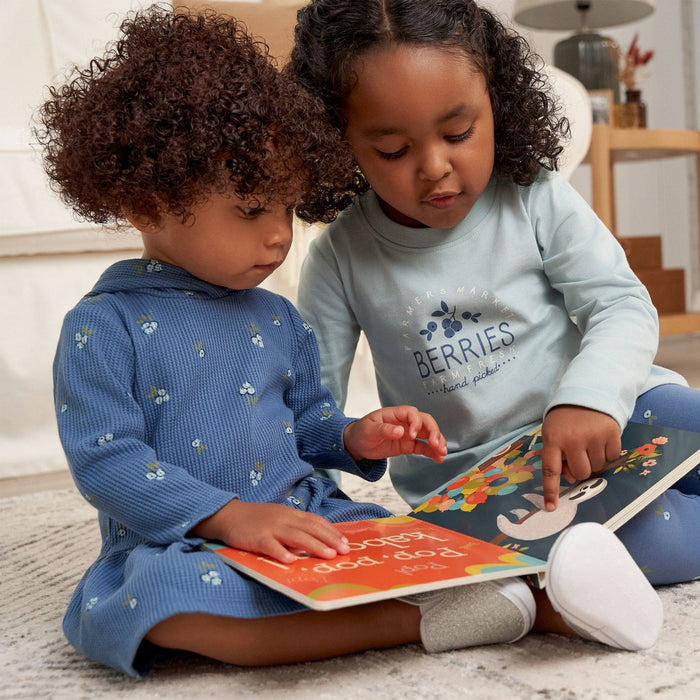 Two young girls seated on the floor, engrossed in reading a book together, sharing a moment of joy and discovery