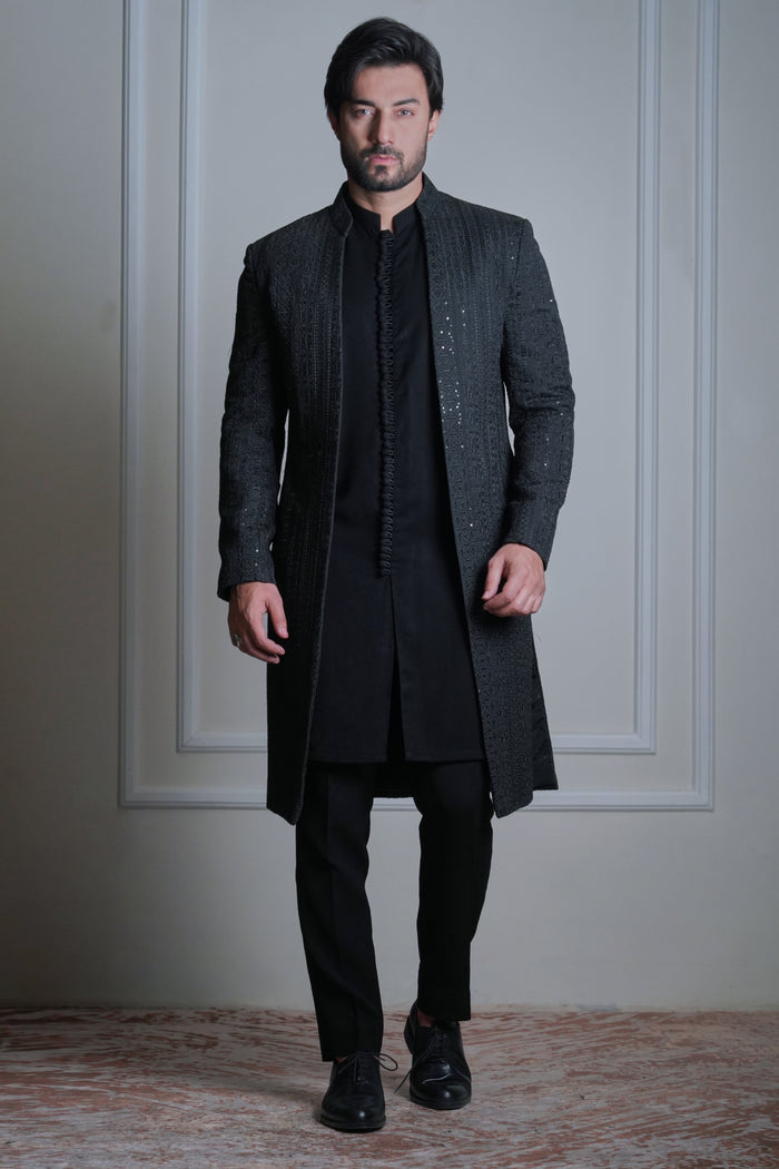 Male model wearing a black sherwani by Arsalan Iqbal, modern formal ethnic menswear in an elegant indoor setting