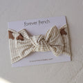 The Bamboo Head Wrap | Teddy by forever french baby features a cream and beige plaid design with small teddy bear prints, shown on branded packaging labeled "forever french baby" and "foreverfrenchbaby.com" on a textured surface.