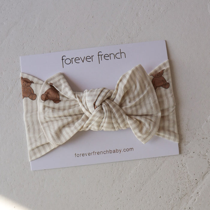 The Bamboo Head Wrap | Teddy by forever french baby features a cream and beige plaid design with small teddy bear prints, shown on branded packaging labeled "forever french baby" and "foreverfrenchbaby.com" on a textured surface.