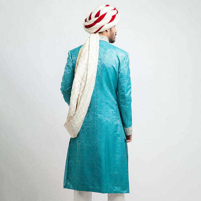 Rear view of an Arsalan Iqbal teal paisley jamawar sherwani showing the tailored fit and the long, draped tail of a white and red brocade turban.