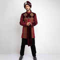 Full-length studio shot of an Arsalan Iqbal deep maroon velvet form-fitted sherwani featuring asymmetrical metallic buttons and a coordinated maroon turban.