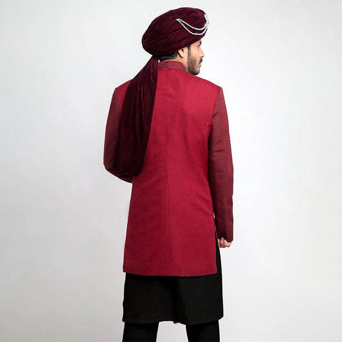 Full-length view of an Arsalan Iqbal burgundy sherwani featuring a maroon velvet chest panel with intricate gold and orange geometric embroidery, paired with a matching velvet turban and black trousers.