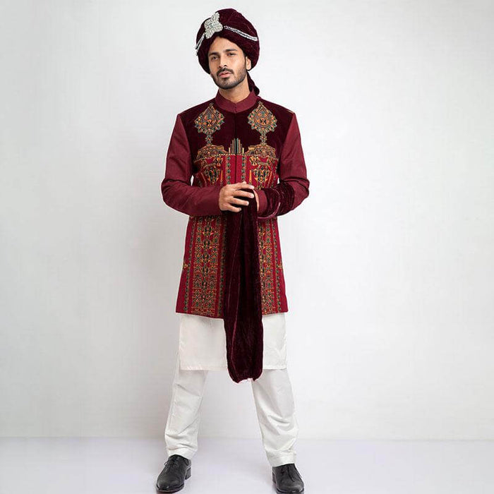 Portrait of a man in an Arsalan Iqbal cream jamawar sherwani with gold embroidered collar and cuffs, paired with a vibrant red and gold polka dot silk turban and matching shawl.