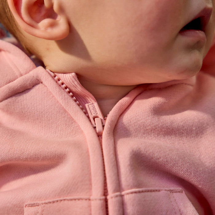 Close-up of a child wearing a dusty pink zip-up hoodie, showing the fabric texture, zipper pull, and part of the ear and mouth.