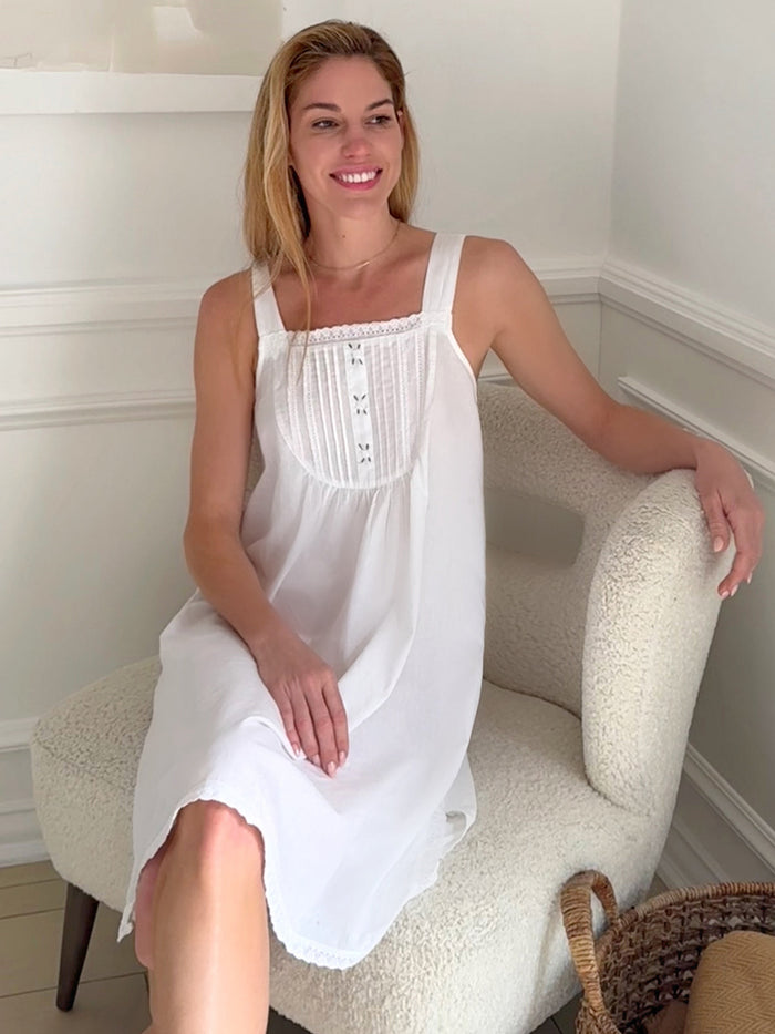 Woman wearing a white dress sitting on a chair in a room with a neutral color scheme.