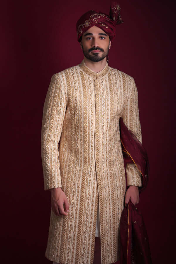 Arsalan Iqbal luxury cream and gold sherwani featuring vertical chevron embroidery and floral panels, paired with a maroon embroidered turban and shawl.