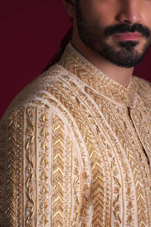 Arsalan Iqbal golden chevron sherwani featuring gold tilla thread-work, architectural chevron patterns, and delicate floral leaf borders on a cream silk base.