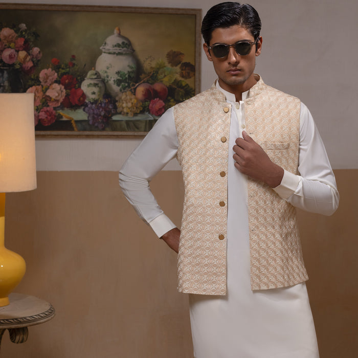 Arsalan Iqbal Light Gold Embroidered Waistcoat with IronEZ Kurta & Pyjama Set – man wearing a light gold heavily embroidered sleeveless waistcoat with gold button closure over a crisp white full-sleeve kurta, paired with matching white straight-cut pyjama, accessorized with sunglasses, styled in a warm classic indoor setting