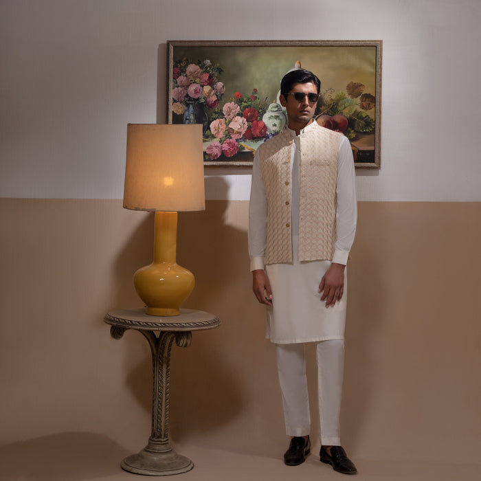 Arsalan Iqbal Light Gold Embroidered Waistcoat with IronEZ Kurta & Pyjama Set  man wearing a light gold heavily embroidered sleeveless waistcoat with gold button closure over a crisp white full-sleeve kurta, paired with matching white straight-cut pyjama, accessorized with sunglasses, styled in a warm classic indoor setting