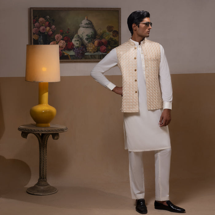 Arsalan Iqbal Light Gold Embroidered Waistcoat with IronEZ Kurta & Pyjama Set  man wearing a light gold heavily embroidered sleeveless waistcoat with gold button closure over a crisp white full-sleeve kurta, paired with matching white straight-cut pyjama, accessorized with sunglasses, styled in a warm classic indoor setting
