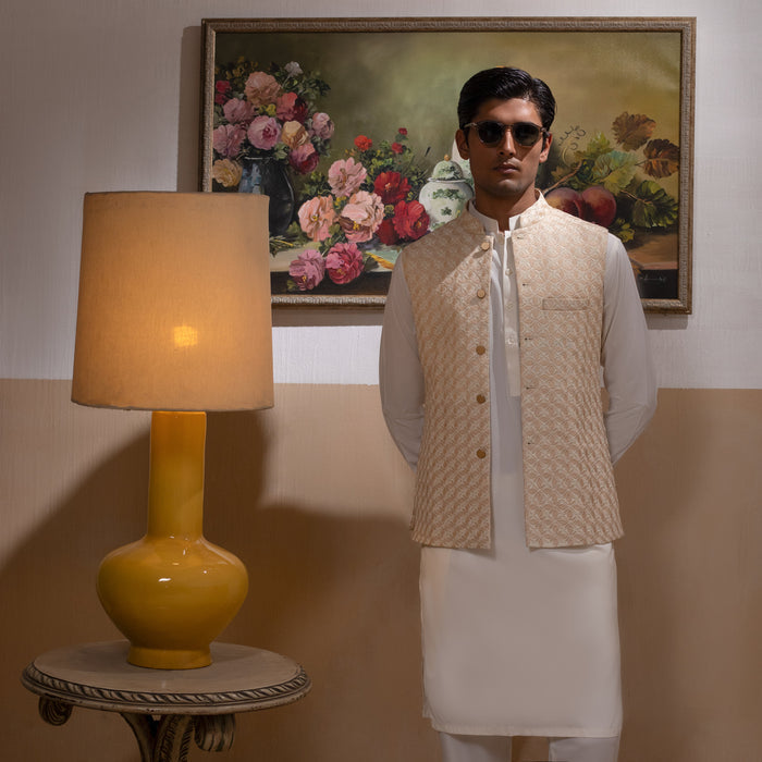 Arsalan Iqbal Light Gold Embroidered Waistcoat with IronEZ Kurta & Pyjama Set man wearing a light gold heavily embroidered sleeveless waistcoat with gold button closure over a crisp white full-sleeve kurta, paired with matching white straight-cut pyjama, accessorized with sunglasses, styled in a warm classic indoor setting