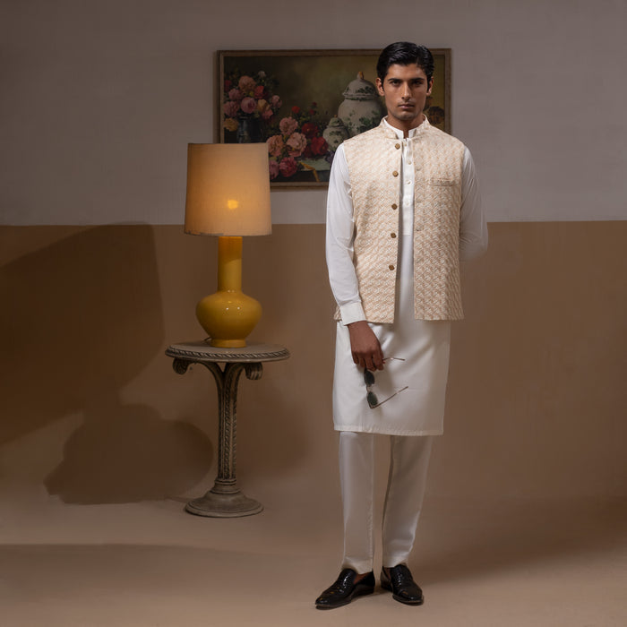 Arsalan Iqbal Light Gold Embroidered Waistcoat with IronEZ Kurta & Pyjama Set – man wearing a light gold heavily embroidered sleeveless waistcoat with gold button closure over a crisp white full-sleeve kurta, paired with matching white straight-cut pyjama, accessorized with sunglasses, styled in a warm classic indoor setting
