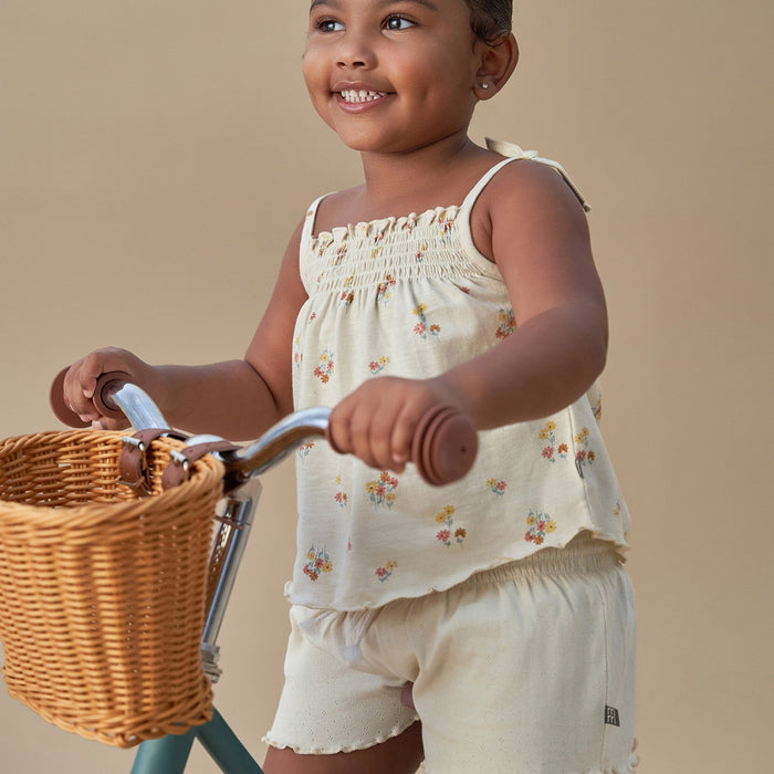 Child in a floral dress standing next to a bicycle with a basket on a beige background