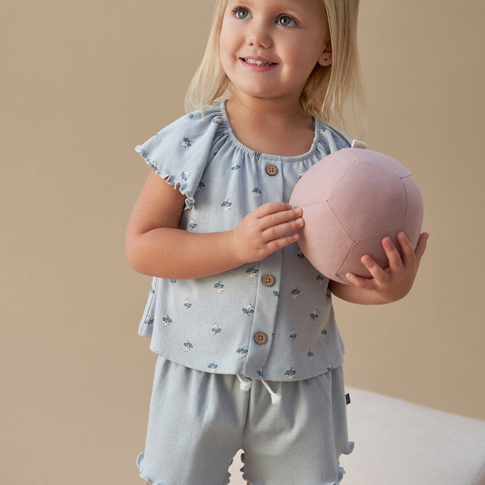 Young girl holding a pink ball wearing a light blue outfit with ruffled sleeves against a beige background