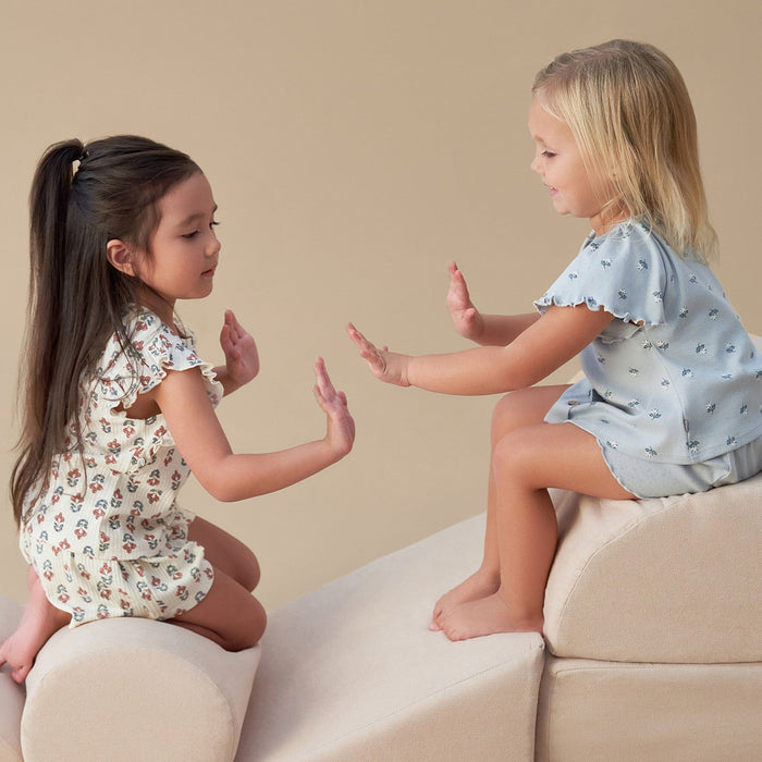 Two young girls playing with their hands on a beige couch.
