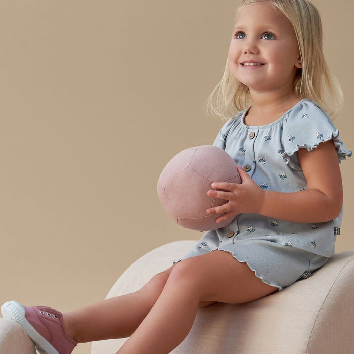 Young girl holding a pink ball, wearing a light blue outfit with a beige background