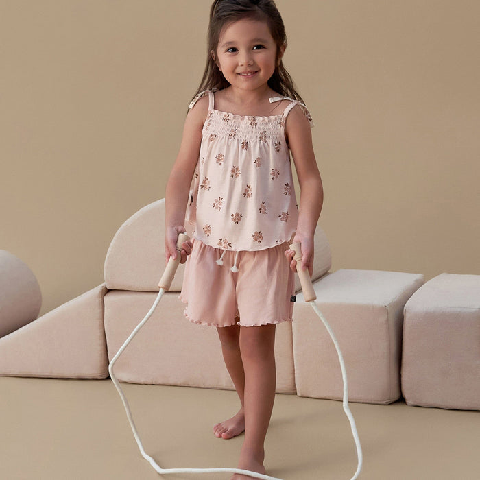 Young girl in a floral top and shorts holding a jump rope against a beige background
