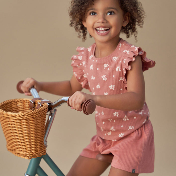 Child in pink floral outfit riding a bicycle with a wicker basket on a beige background