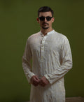 Man wearing Arsalan Iqbal's Off-White Ivory Kurta with allover silver and gold sequin embroidery, styled with black sunglasses against a deep green background