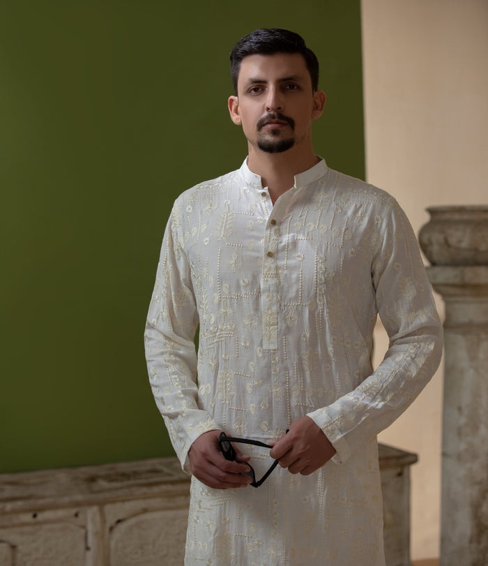 Man wearing Arsalan Iqbal's Off-White Ivory Kurta with allover silver and gold sequin embroidery, styled with black sunglasses against a deep green background