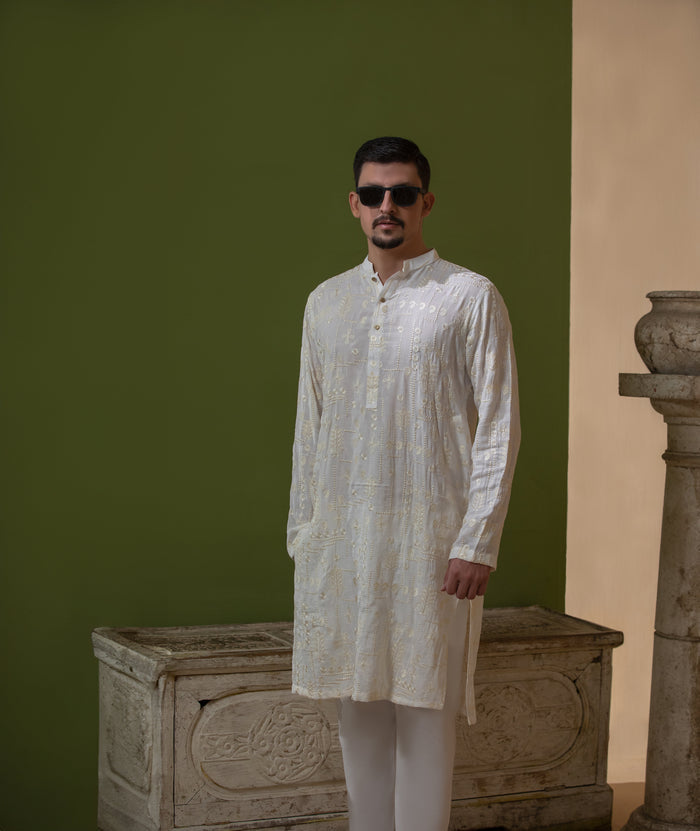 Man wearing Arsalan Iqbal's Off-White Ivory Kurta with allover silver and gold sequin embroidery, styled with black sunglasses against a deep green background