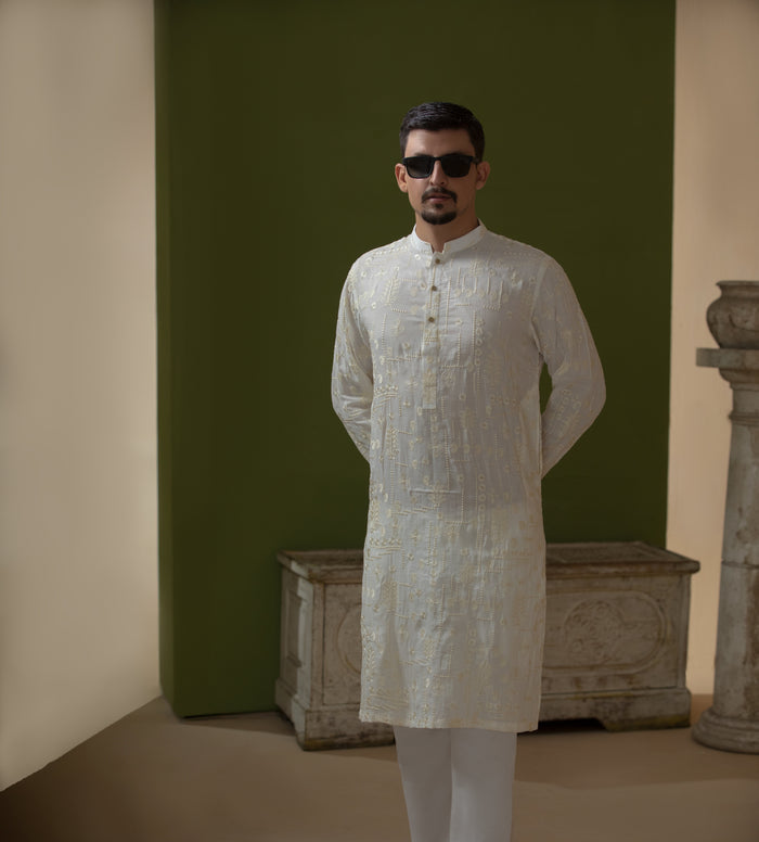 Man wearing Arsalan Iqbal's Off-White Ivory Kurta with allover silver and gold sequin embroidery, styled with black sunglasses against a deep green background