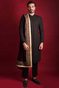 Arsalan Iqbal luxury black sherwani featuring all-over maroon and green micro-embroidery, styled with a heavy maroon velvet shawl with a gold embroidered border and black trousers.
