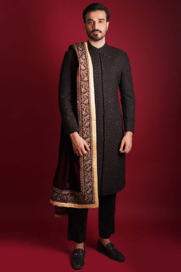 Arsalan Iqbal luxury black sherwani featuring all-over maroon and green micro-embroidery, styled with a heavy maroon velvet shawl with a gold embroidered border and black trousers.