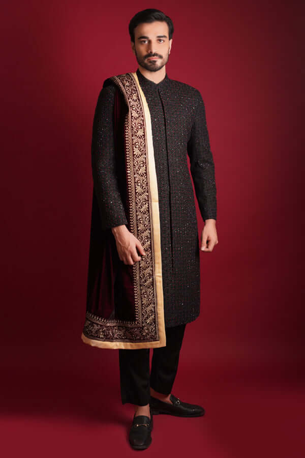 Arsalan Iqbal luxury black sherwani with maroon and green micro-embroidery, paired with a draped maroon velvet shawl featuring a heavy golden tilla border, styled with black trousers and bit-loafers.