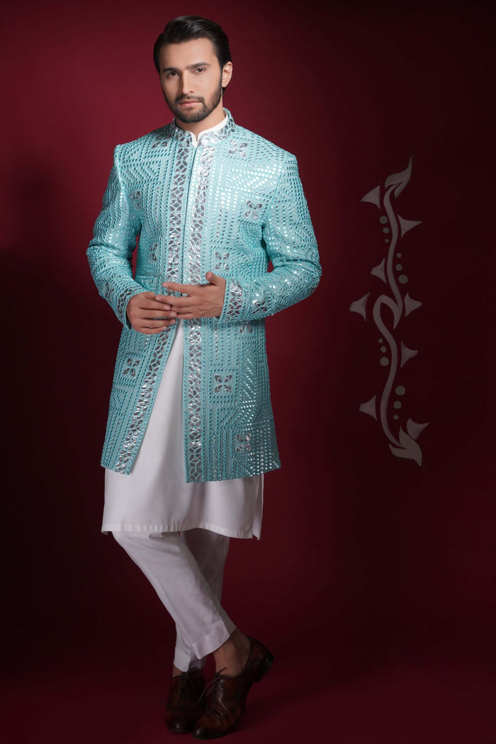Arsalan Iqbal ice-blue prince coat with silver geometric mirror-work, featuring a model in a cross-legged pose with white traditional layers.