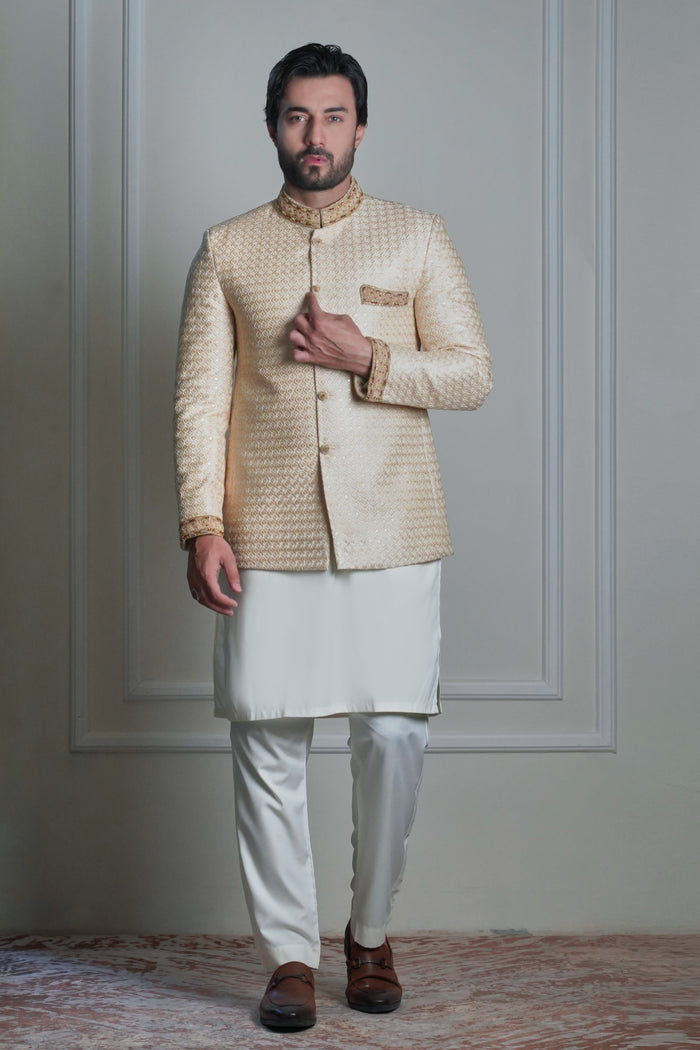 Men’s ivory jacquard prince coat with gold embroidered collar and cuffs, worn by male model standing indoors.