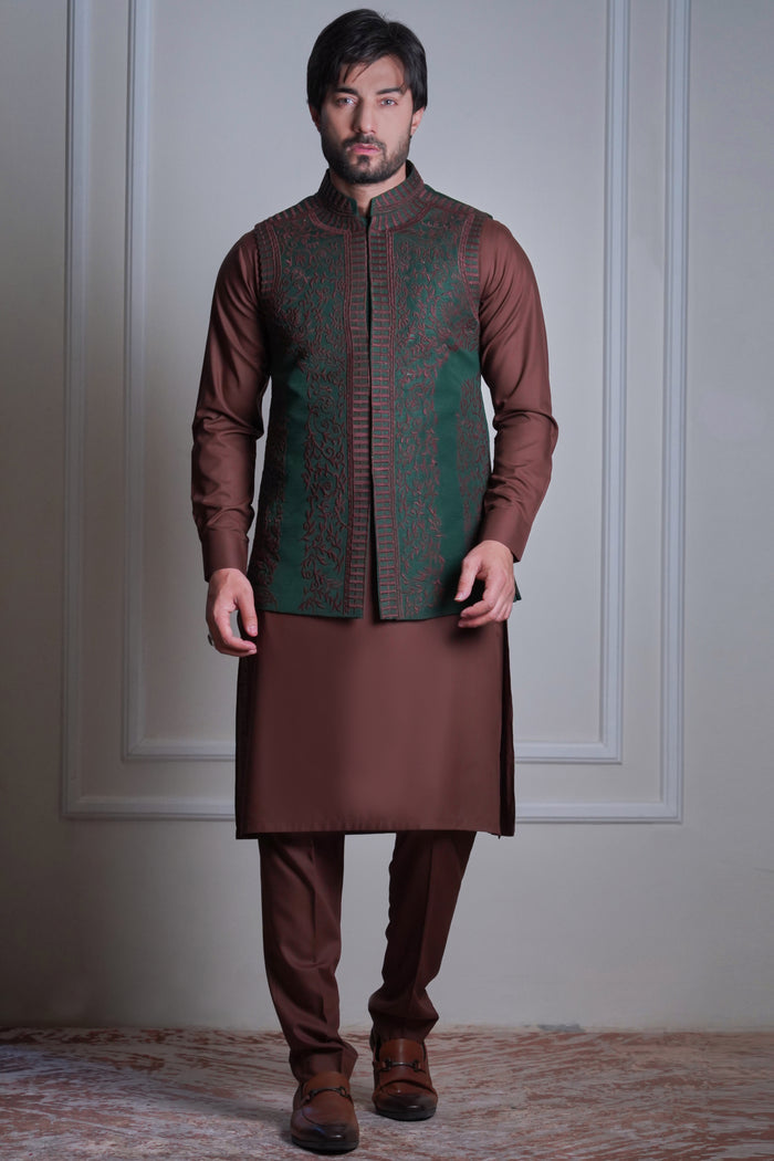 A man wearing a regal maroon Arsalan Iqbal waistcoat with intricate silver embroidery and mirror work, layered over a sleek black kurta and trousers.