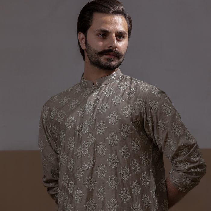 Arsalan Iqbal Beige Classic Chikankari Kurta Pyjama  man wearing a beige full sleeve kurta with intricate white chikankari floral embroidery, mandarin collar, and a relaxed tailored fit, styled in a warm indoor setting