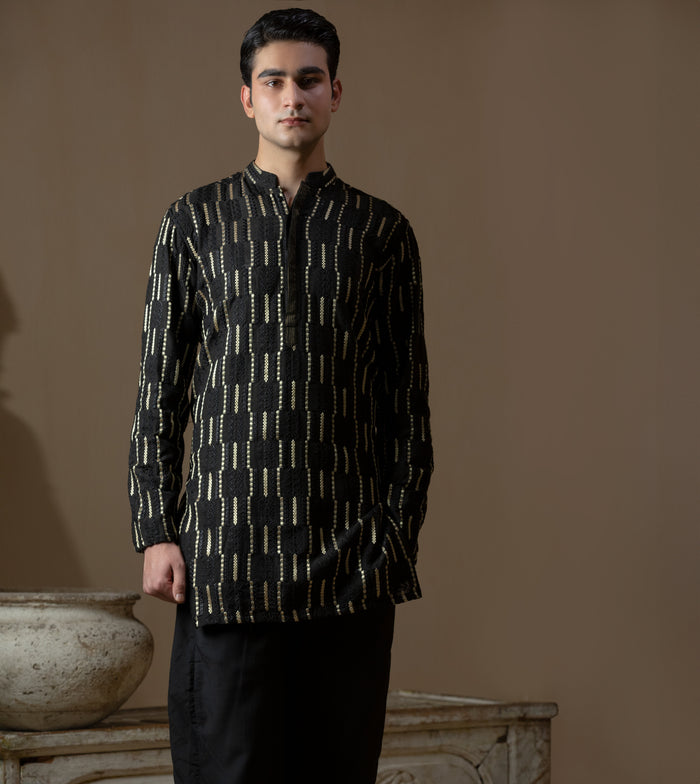 Man wearing Arsalan Iqbal's Black Kurta with allover gold metallic embroidery, styled with sunglasses and a silver watch against a dark background