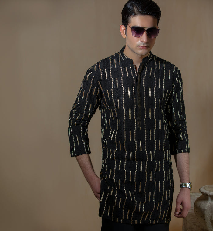 Man wearing Arsalan Iqbal's Black Kurta with allover gold metallic embroidery, styled with sunglasses and a silver watch against a dark background