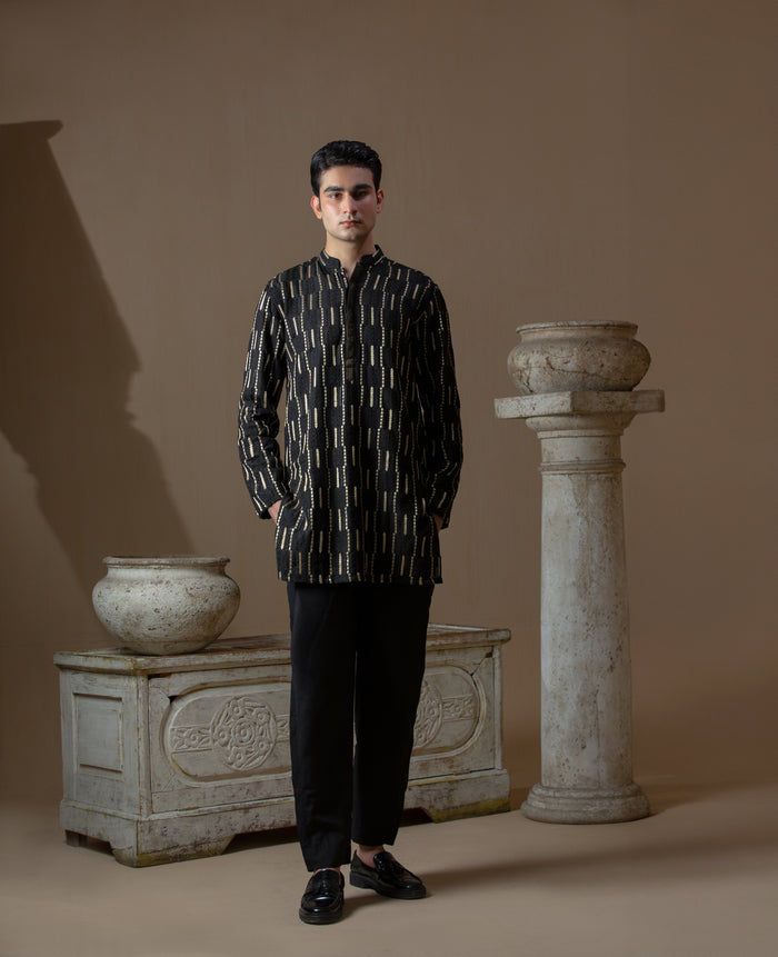 Man wearing Arsalan Iqbal's Black Kurta with allover gold metallic embroidery, styled with sunglasses and a silver watch against a dark background