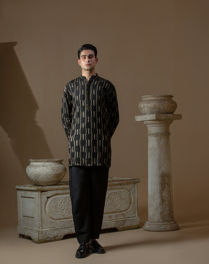 Man wearing Arsalan Iqbal's Black Kurta with allover gold metallic embroidery, styled with sunglasses and a silver watch against a dark background