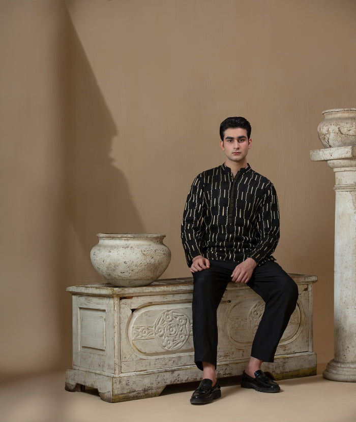 Man wearing Arsalan Iqbal's Black Kurta with allover gold metallic embroidery, styled with sunglasses and a silver watch against a dark background