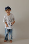A young child wears the forever french baby T-Shirt & Pant Set | ff Los Angeles—a playful, angel-graphic white tee and blue gingham pants—perfect for expressing LA-inspired kids style.