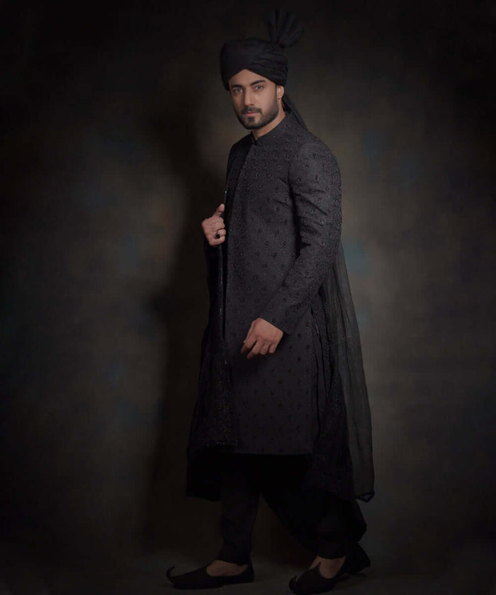Side profile view of Arsalan Iqbal midnight black luxury sherwani featuring spaced-out tonal motifs, styled with a high-pleated black turban, matching trousers, and traditional khussa shoes.