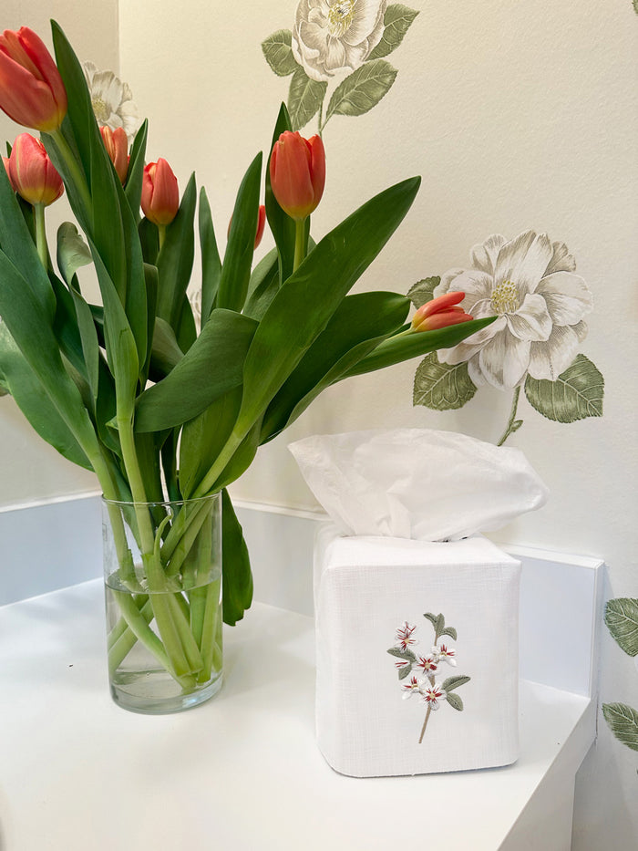 Red tulips in a vase on a white surface with floral wallpaper in the background