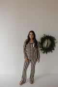 A woman stands barefoot in the forever french baby Women's Bamboo Button Up Lounge Set in Midnight Stripe, set against a plain white wall with a green wreath beside her.