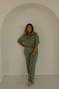 A woman with shoulder-length hair smiles under a white arch, wearing the forever french baby Women's Boxy Tee Lounge Set in Santa Checkerboard. She stands with one hand on her hip against a plain, neutral background.